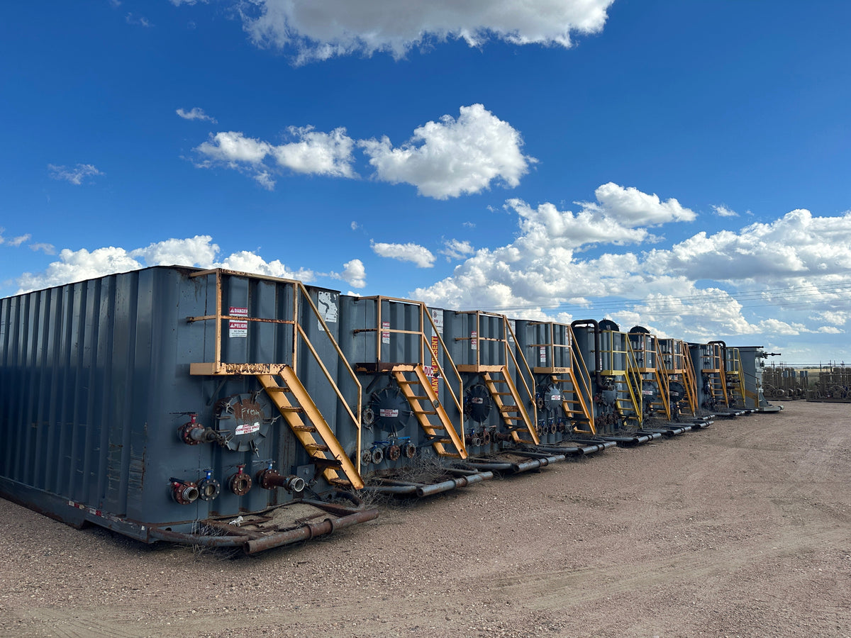 Row of used frac tanks against a backdrop of the sky