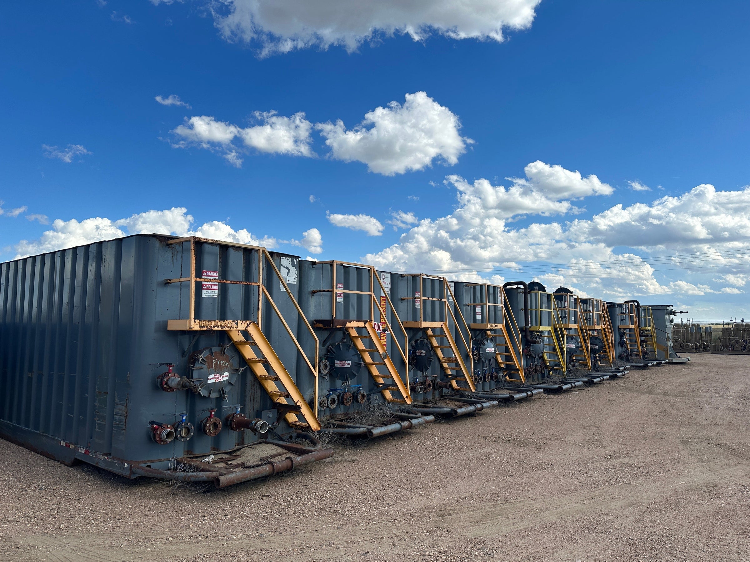 Row of used frac tanks against a backdrop of the sky